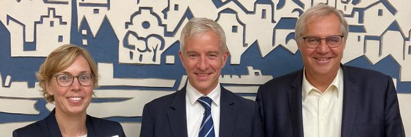 Rowena Sandmeier (FD-Leitung Stadtentwicklung) Hayo Nadler (Highstreet Group) Stephan Dose (Bürgermeister Stadt Schleswig) vor einem Bild der Stadt Schleswig