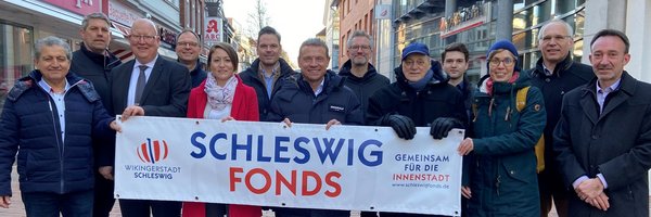 Mitglieder des Schleswig Fonds halten stehen in der Innenstadt mit einem Plakat "Schleswig Fonds"