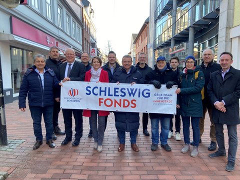 Mitglieder des Schleswig Fonds halten stehen in der Innenstadt mit einem Plakat "Schleswig Fonds"