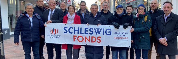 Mitglieder des Schleswig Fonds halten stehen in der Innenstadt mit einem Plakat "Schleswig Fonds"