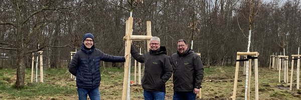 Jens Bagehorn-Delor, Stadt Schleswig, Öffentliches Grün sowie Sven Schnoor und Sven Hörmann, Firma Schnoor Garten- und Landschaftsbau, Schuby stehen vor einer Baumgruppe