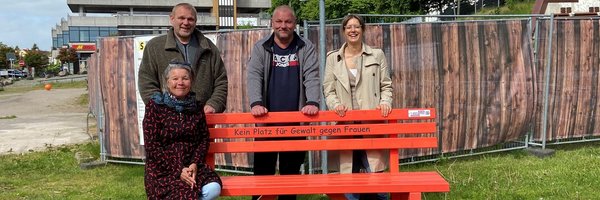 Andrea Cunow, Gleichstellungsbeauftragte Stadt Schleswig; Justizvollzugsbeamte Frank Speth und Hartmut Will sowie Josephine Schäfer aus dem Fachdienst Stadtplanung sitzen bzw. stehen hinter der orangenfarbenen Bank mit der Aufschrift Keine Platz für Gewalt gegen Frauen