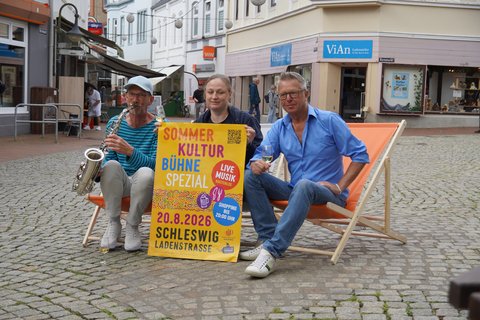 Musiker Jonny Möller, Sabrina Erck vom Stadtmarketing und Harry Ober vom Wein- & Whisky-Depot freuen sich auf die Veranstaltung sitzen in der Innenstadt auf Klappstühlen