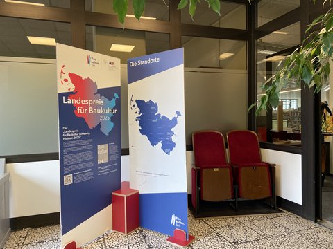 Im Eingangsbereich der Stadtbücherei weisen große Pappaufsteller auf die Ausstellung Landespreis für Baukultur 25.–30.03.2026 hin