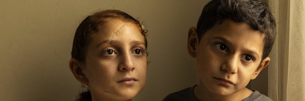 Zwei Kinder. Das eine hat seinen Arm um das andere gelegt. 