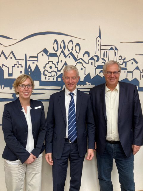 Rowena Sandmeier (FD-Leitung Stadtentwicklung) Hayo Nadler (Highstreet Group) Stephan Dose (Bürgermeister Stadt Schleswig) vor einem Bild der Stadt Schleswig