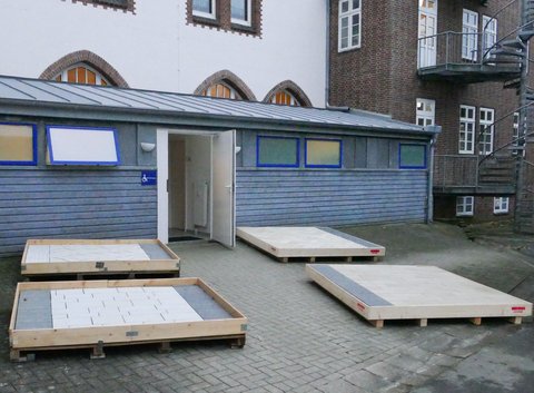 Materialproben auf palettenähnlichen Unterkonstruktionen, die zur Veranschaulichung der geplanten Pflasterung dienen