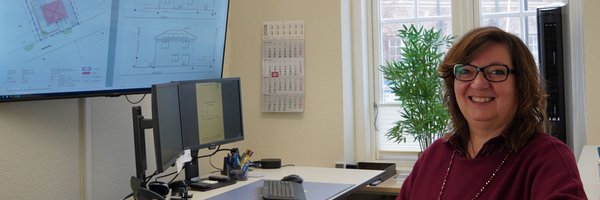 Anja Friedrich stehend an ihrem Arbeitsplatz, vor ihr der höhenverstellbare Schreibtisch und zwei Bildschirme