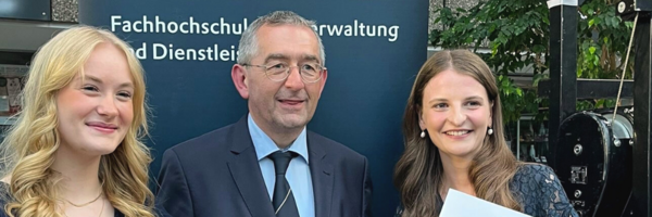 Norbert Krüger (Ausbildungsverantwortlicher) mit den Absolventinnen Eilien Sievers (l.) und Jule Böttcher vor einem Banner der FHVD
