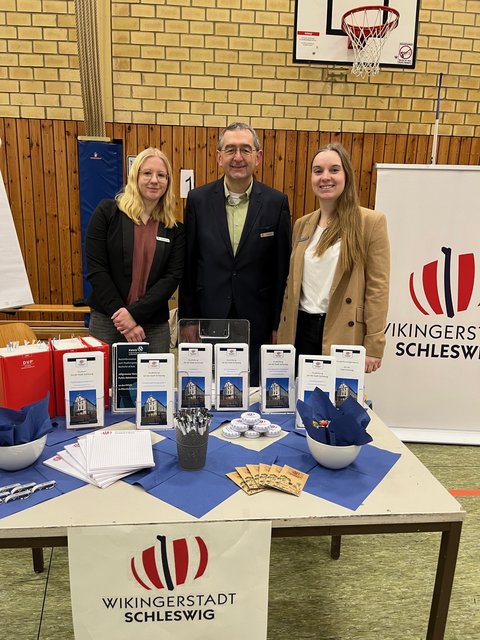 Anna Puhlmann, Auszubildende zur Erzieherin in praxisintegrierter Form aus der Kita Bildungsbox und Norbert Krüger sowie Julia Sell aus dem Fachdienst Personal hinter einem Messestand