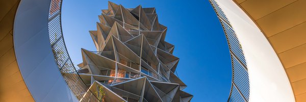 Ein Geometrisch abstrakt geformtes Gebäude, von unten aus einem Runden Treppenaufgang fotografiert. 