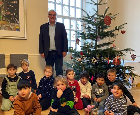 Ein Gruppenfoto von Stephan Dose mit Kindern eines städtischen Kindergartens beim Weihnachtsbaumschmücken im Rathaus.