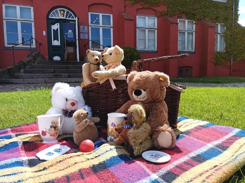 Teddybären auf eine Decke mit Miniaturgeschirr auf dem Rasen vor dem Stadtmuseum