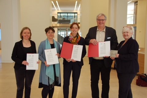 Das Bild zeigt fünf Personen, welche Schriftstücke vor sich in Richtung der Kamera halten. Von links nach rechts stehen dort Frau Dr. Ute Lemm, Monika Heinold und Karin Prien. Daneben stehen der Bürgermeister der Stadt Schleswig Stephan Dose und die Fachbereichsleiterin des Fachbereichs Bildung, Kultur und Ordnung der Stadt Schleswig Frau Dr. Julia Pfannkuch.