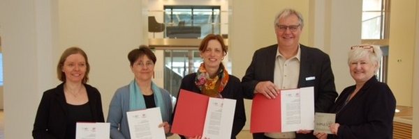 Das Bild zeigt fünf Personen, welche Schriftstücke vor sich in Richtung der Kamera halten. Von links nach rechts stehen dort Frau Dr. Ute Lemm, Monika Heinold und Karin Prien. Daneben stehen der Bürgermeister der Stadt Schleswig Stephan Dose und die Fachbereichsleiterin des Fachbereichs Bildung, Kultur und Ordnung der Stadt Schleswig Frau Dr. Julia Pfannkuch.