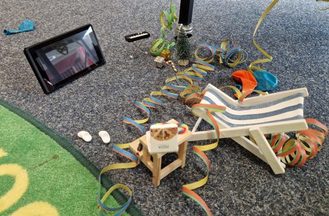 Liegestuhl, Luftballons, Pizza, Musik und Fernseher im Miniaturformat auf dem Büchereiboden