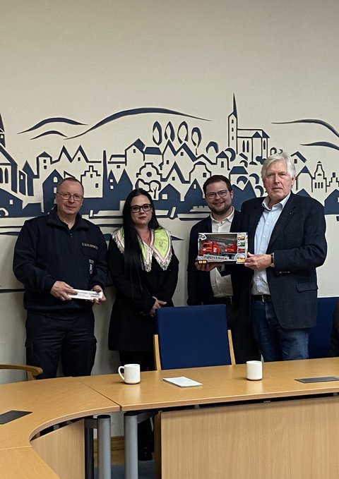 Sönke Schlossmacher, Bettina Schiermeyer Jonas Kähler und Rainer Raup halten ein Feuerwehrwagen im Sitzungszimmer in der Hand