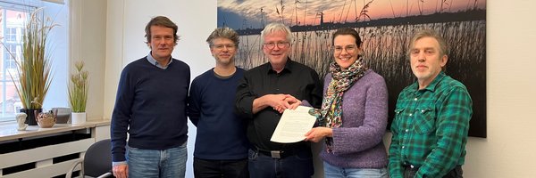 Vertragsunterzeichnung Energiegemeinschaft Schlei und Stadt Schleswig: Michael Struck, Robert Wünsch, Bernward Völmicke (Stadt Schleswig), Cornelia Sperling, Peter Kieseritzky stehen vor einem großen Bild mit Abendlandschaft
