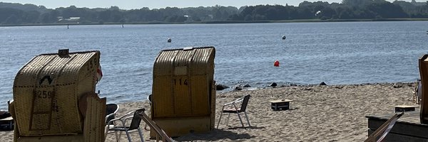 Bild zeigt das Luisenbad mit Blick auf Strandkörbe und die Schlei. Rechts ist Gastronomie zu sehen.