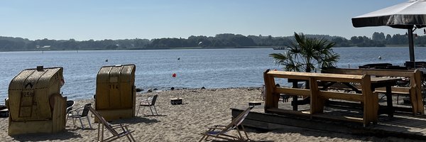 Bild zeigt das Luisenbad mit Blick auf Strandkörbe und die Schlei. Rechts ist Gastronomie zu sehen.