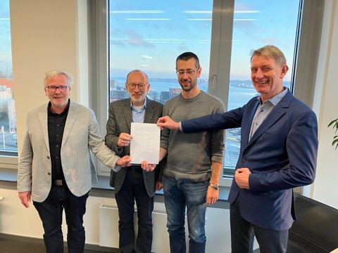 Bernward Völmicke, Stadt Schleswig, Bernd Hannemann, Diakonie Stiftung Schleswig-Holstein, Alexander Opitz, Stadt Schleswig, Kay-Gunnar Rohwer, Diakonie Stiftung Schleswig-Holstein halten einen unterschriebenen  Kaufvertrag in der Hand