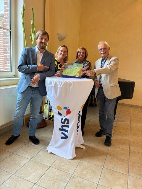 Florentin Viebig, Liisa Suhr und Jennifer Siessegger (vhs) sowie Horst Quante (LQW-Gutachter) halten die LQW-Kachel an einem Stehtisch in die Kamera