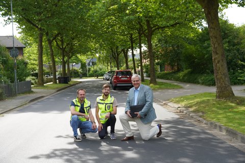 Torben Krüger, Fabian Hundertmark und Bürgermeister Stephan Dose knien auf der sanierten Kastanienallee