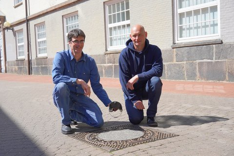 Arne Clemens und Andreas Gens von den Stadtwerken SH mit einer Rückstauklappe vor dem Rathaus