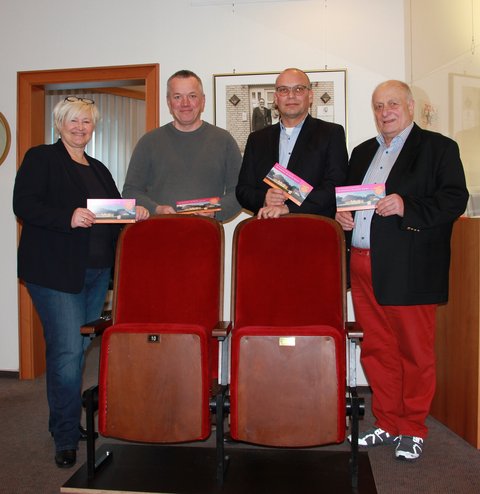 Das Bild zeigt (v.l.n.r.) die Fachbereichsleitung des Fachbereichs Bildung, Kultur und Ordnung Frau Dr. Julia Pfannkuch, Herrn Christian Jensen von der Tischlerei Jensen und die Rechtsanwälte und Notare Karsten und Frank Noetzel. Gemeinsam stehen sie hinter den überreichten Theaterstuhl-Tandems und halten den neuen Spendenflyer "Das Kulturhaus. Die Zukunft. Sind wir." vor.
