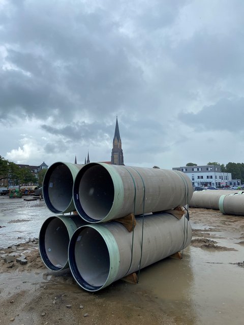 Vier große Rohre auf einer Baustelle im Regen, der Dom im Hintergrund