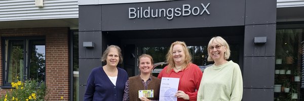 Übergabe Preisgeld Kita BildungsBox: B. Hindrichsen, F. Großkopf und S. Struve von der Kita BildungsBox sowie N. Wiemeier (Stadt Schleswig) vor dem Gebäude der Kita BildungsBox mit einem Fahrrad im Vordergrund