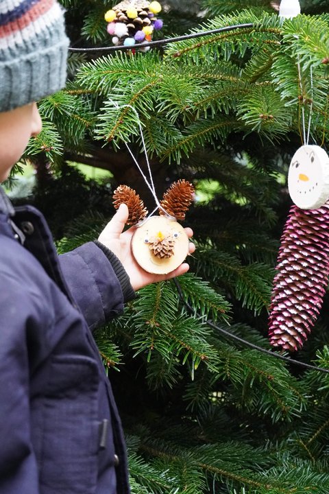 Ein Kind beim Weihnachtsbaumschmücken mit einem gebastelten Rentier-Weihnachtsbaumanhänger.