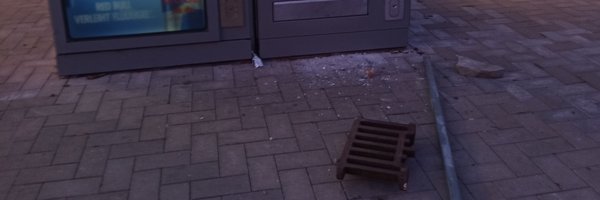 Beschädigter Snackautomat mit gesprungener Scheibe, davor Eisenstange und Gullydeckel auf dem Boden