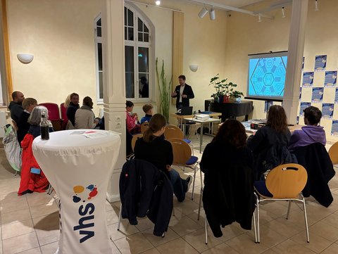 Frank Martis im Vordergrund erklärt den Teilnehmenden das Demokratiespiel Quararo auf einem Bildschirm im Hintergrund