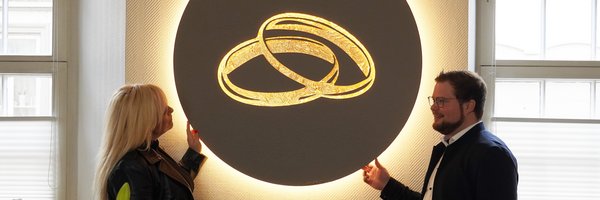 Künstlerin Kathrin Geller und Bürgermeister Jonas Kähler vor dem beleuchteten Kunstobjekt im Trauzimmer, das zwei goldene Ringe zeigt.