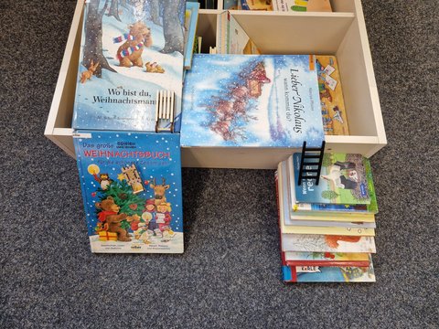 Weihnachtskinderbücher liegen in und vor eine Kiste ebenso wie ein Bücherstapel auf dem eine kleine Leiter gesetzt wurde