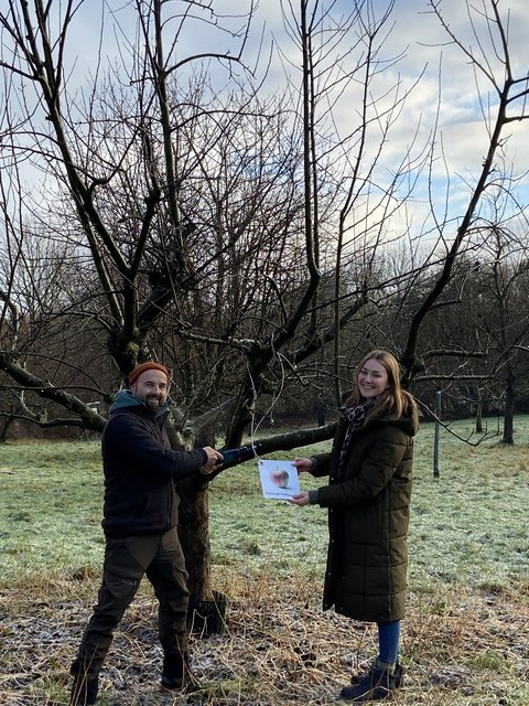 Miklas Staiger und Maren Thiesen stehen vor einem Obstbaum mit Baumschere und Schild