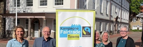 Das Foto zeigt aus dem Steuerungsgruppen-Team Sina Clorius (Ratsversammlung), Matthias Hertel und Ute Ulrich (Verein zur Förderung des fairen Handels Schleswig e. V.) Maren Korban und Inke Asmussen (beide Ratsversammlung) mit einem Aufsteller "Wir machen mit" vor dem Schleswiger Rathaus