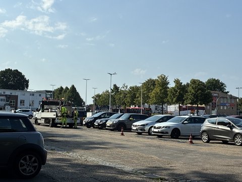 Parkende Autos und ein Straßensanierungsfahrzeug mit zwei Mitarbeitenden