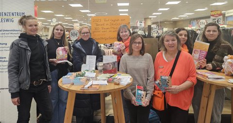 Alix Voland, Heidi Thiel, Corinna Philipsen, Andrea Cunow, Annika Bruhn, Hanna Pikowski, Christiane Schunter und Julia Brüggen vor einem Schaufenster im Schleicenter mit Brötchentüten in der Hand auf den steht: Gewalt kommt nicht in die Tüte
