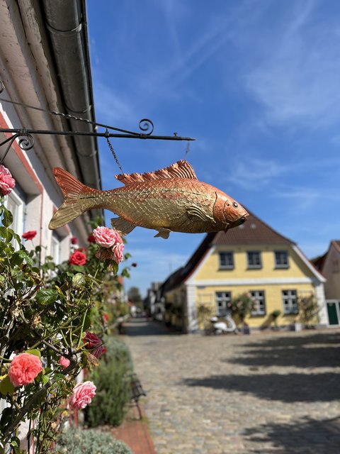 Gold-Orangene Fischfigur, die an einer Hauswand auf dem Holm in Schleswig hängt