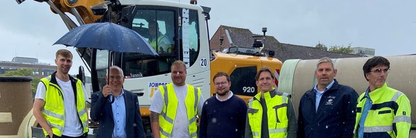 Thore Stamm (Johannssen Straßen-, Hoch- & Tiefbau GmbH), Stefan Wesemann (IHK), Martin Gast (Fa. Johannssen), Jonas Kähler (Stadt Schleswig), Marco Armgort (Masuch + Olbrisch Ingenieurgesellschaft für das Bauwesen mbH), Helge Schütze (Stadtmarketing) und Arne Clemens (Schleswiger Stadtwerke Abwasserentsorgung - Eigenbetreib der Stadt Schleswig) auf der Baustelle am Schwarzen Weg. Im Hintergrund ein Bagger.
