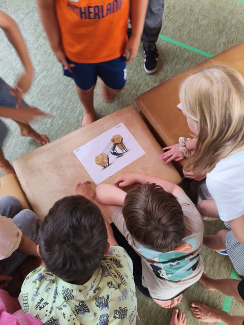 Kinder stehen und sitzen am Tisch und betrachten ein Bild