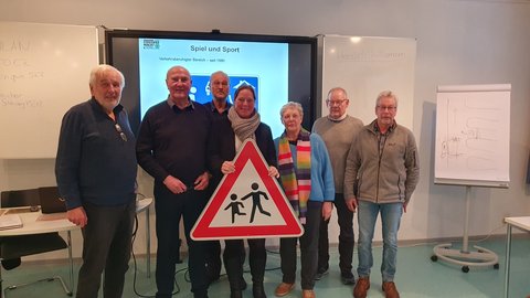 Verkehrssicherheitskurs „Alte Hasen – neue Regeln“ - v.l.n.r.: O. Kaufhold (Teilnehmer), R. Greulich (Landesverkehrswacht, Dozent) C. Schmolling (Seniorenbeirat), S. Hein (Kreisverkehrswacht), R. Henningsen, H. Seefeldt und J. Redmann (Teilnehmende) vor einer Leinwand und mit einem Verkehrsschild in der Hand