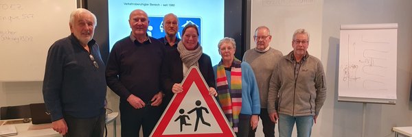 Verkehrssicherheitskurs „Alte Hasen – neue Regeln“ - v.l.n.r.: O. Kaufhold (Teilnehmer), R. Greulich (Landesverkehrswacht, Dozent) C. Schmolling (Seniorenbeirat), S. Hein (Kreisverkehrswacht), R. Henningsen, H. Seefeldt und J. Redmann (Teilnehmende) vor einer Leinwand und mit einem Verkehrsschild in der Hand