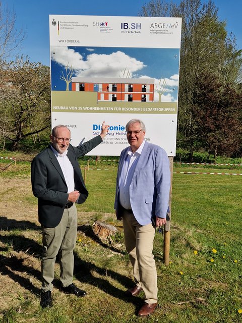 Spatenstich Housing first im Ansgarweg - Bernd Hannemann (Diakonie Schleswig-Holstein) und Stephan Dose (Stadt Schleswig) vor einem großen Bauschild