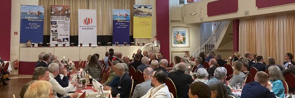 Blick auf Gäste am Tisch, die auf ein Rednerpult schauen