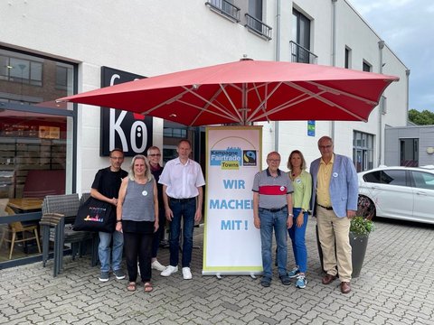 Auf dem Foto sind (von links nach rechts): Jörg Ziemert (Ziemert Folienbeschriftungen), Maren Korban und Inke Asmussen (Steuerungsgruppe Fairtrade-Stadt), Klaus Dieter Lemmermann (Bäckerei Schmidt), Matthias Hertel und Sina Clorius (Steuerungsgruppe Fairtrade-Stadt) sowie Bürgermeister Stephan Dose vor dem Café Kö.