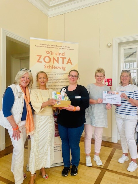 K. Petersen-Nißen (Präsidentin ZONTA Schleswig), K. Suhling (Ordnungsamtsleiterin), H. Hoffmann (Vizepräsidentin ZONTA Schleswig), S. Roß (Bürgervorsteherin), A. Heinrich (stellv. Vors. ZONTA Freundinnen e.V.) vor einem Aufsteller ZONTA