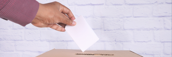 Hand, die einen Stimmzettel in eine Wahlurne tut.